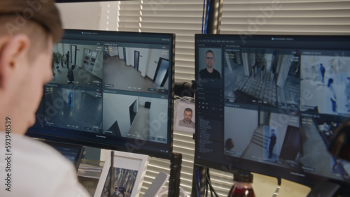 Close up shot of security officer controlling CCTV cameras, using walkie talkie and computers screens showing surveillance cameras footage with modern face scanning system. Concept of social safety.