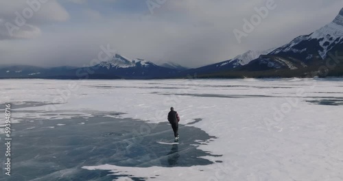 aerial view of man ice skating on frozen abraham lake in alberta, canada