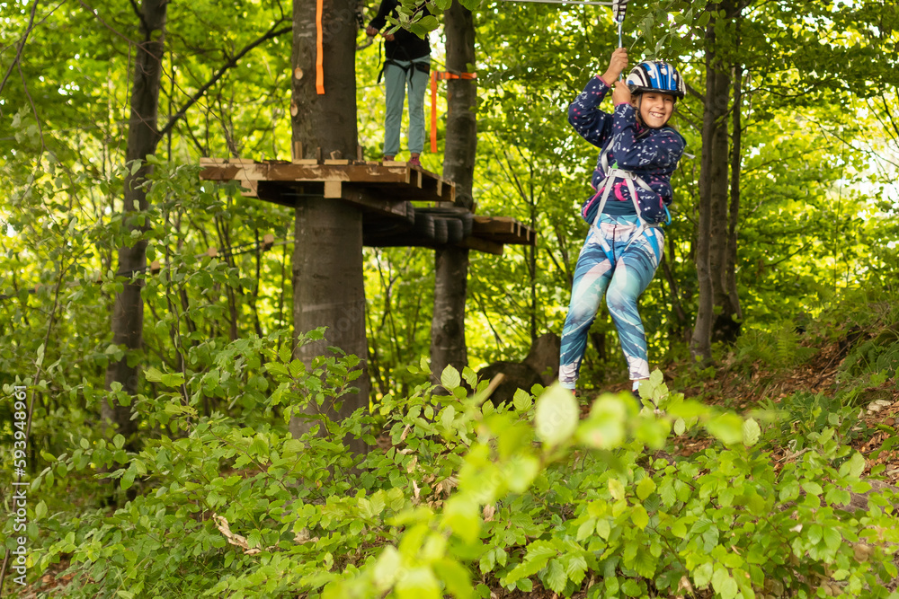 Little girl preschooler wearing full climbing harness having fun time in the rope park using carabiner and other safety equipment. Summer camp activity for kids. Adventure park in the forest Little girl preschooler wearing full climbing harness having fun time in the rope park using carabiner and other safety equipment. Summer camp activity for kids. Adventure park in the forest