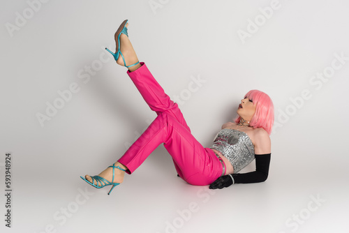 Fotografie Fashionable transgender person in pink wig and sparkling top lying on grey background