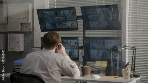 Security operator monitors office CCTV cameras on computers  uses walkie talkie. Modern software showing footage of surveillance cameras on screens. High tech security. Concept of social safety.