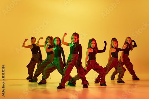 Group of talented kids, autistic children in stylish clothes dancing, performing hip-hop against yellow studio background in neon light. Concept of childhood, hobby, sportive lifestyle