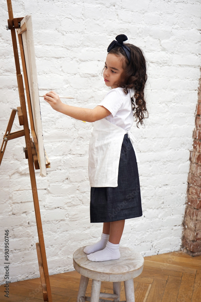 Talented girl artist painting on drawing easel with painting brush. Art school workshop. Vertical orientation. Talented girl artist painting on drawing easel with painting brush. Art school workshop. Vertical orientation.