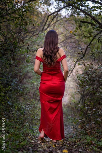 Pretty woman from behind wearing a red dress and walking in the woods