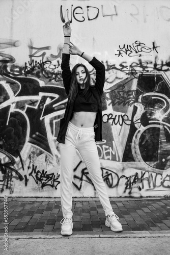 Monochrome shot of the confident pretty female standing in front of the graffiti wall