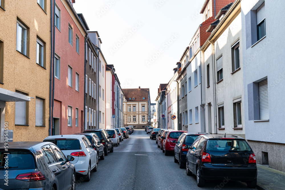 Obraz premium Narrow city lane with cars parked tightly on both sides. Faded colorless sky over residential buildings.