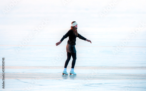 A young happy woman is skating on the transparent ice of the frozen Lake Baikal on a sunny winter day - World-famous figure skater 