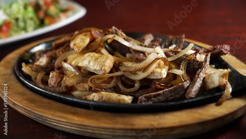 Steam rises from sizzling skillet of combination beef and chicken fajitas with onions and peppers, slider close up 4K photo