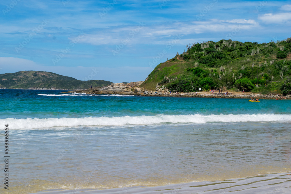 Beautiful Praia das Conchas, close to the city of Cabo Frio, with white sand beaches, blue sky, sea with clean waters in shades of green and blue, with mountains in the background.