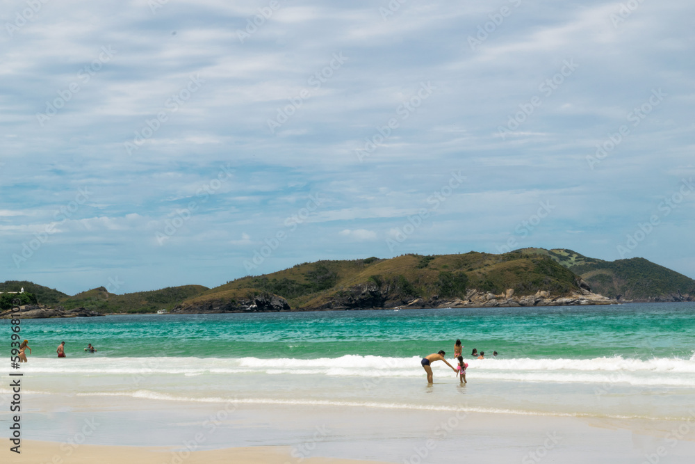 Praia do Forte São Mateus in Cabo Frio, with a beautiful sea of ​​greenish waters and many mountains around, and a beautiful white sand beach.