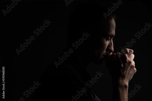 Close up of faithful mature man praying, hands folded in worship to god with head down and eyes closed in religious fervor. Black background. Concept for religion, faith, prayer and spirituality