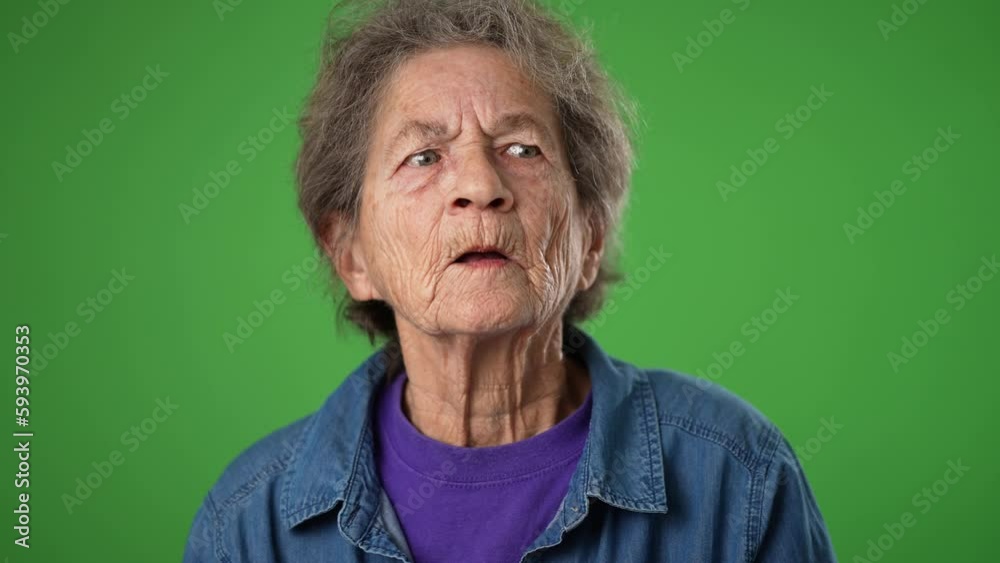 Closeup slow motion funny portrait of happy elderly senior old woman with wrinkled skin and grey hair smiling and look around for friend find meet greet someone posing on green screen background.