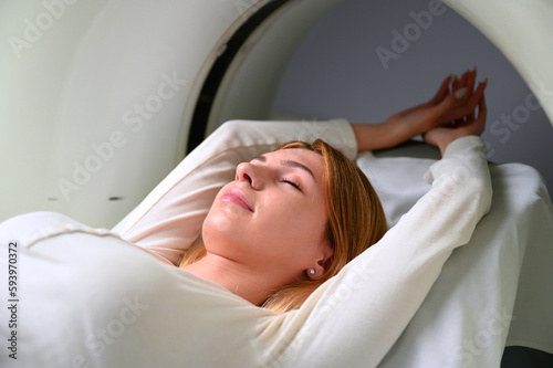 A young woman is undergoing a CT scan procedure. Pretty female in a modern laboratory, lying on the table during CT or MRI. 