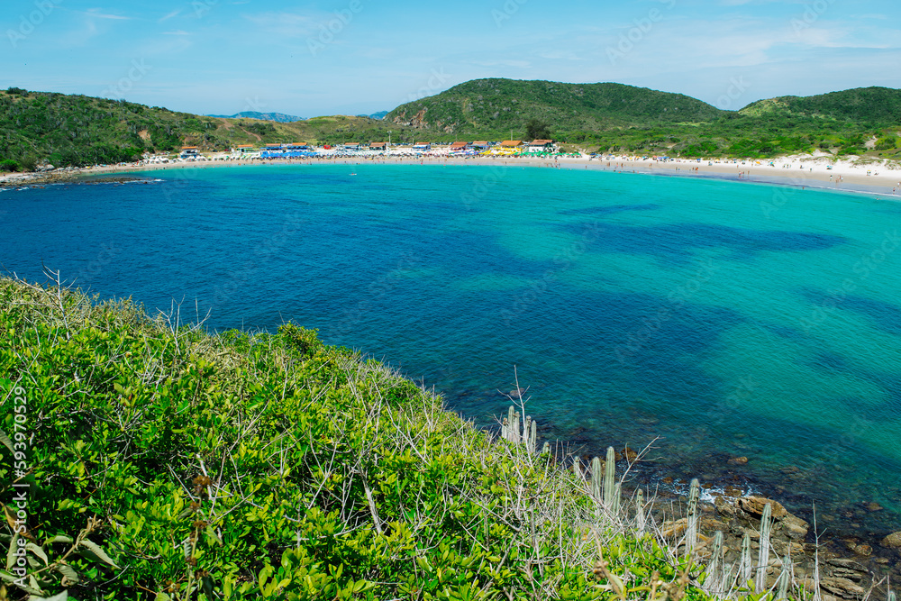 Top view of the beautiful beach of Conchas, close to the city of Cabo Frio, with white sand beaches, blue sky, sea with clean waters and in shades of green and blue, with mountains in the background.