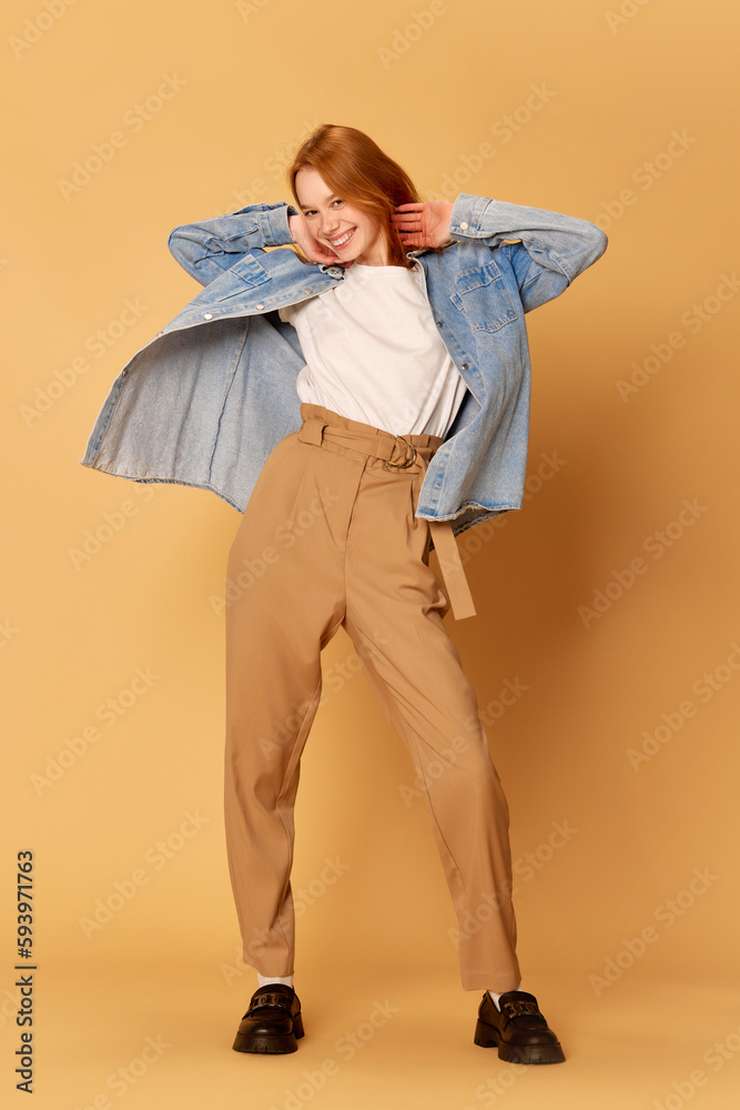 Fototapeta premium One young positive, pretty girl, student wearing casual clothes posing and smiling at camera over ginger background. Happiness, joyful