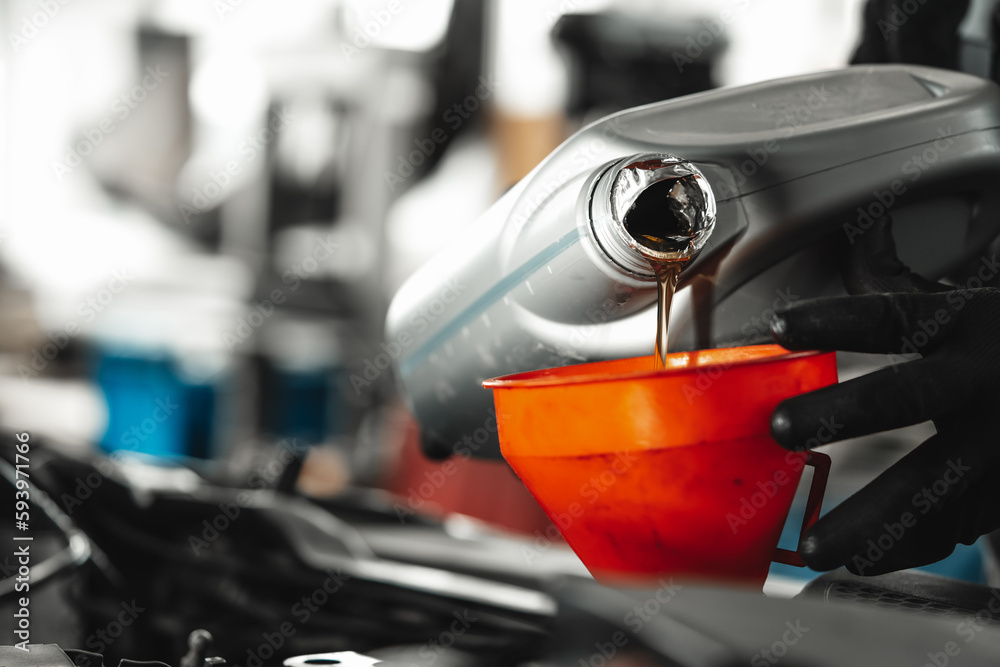 Obraz premium Close up of car service worker pouring new oil into car engine