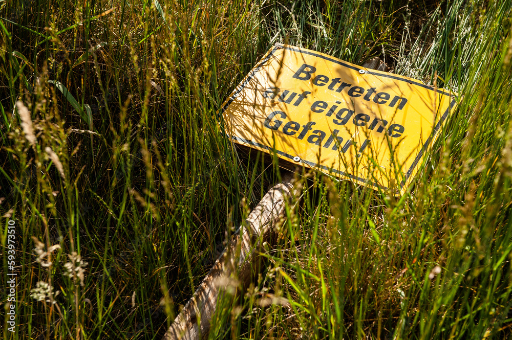 Schild Betreten auf eigene Gefahr liegt im hohen Gras ภาพถ่ายสต็อก Adobe Stock