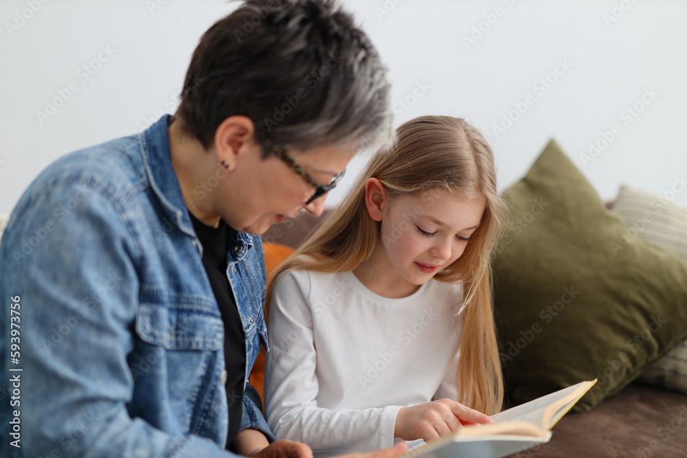 An older woman teaches a child girl to read, reads a story together.