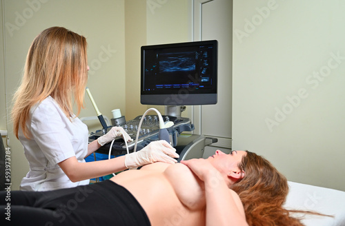 Professional female gynecologist performs an examination of the mammary glands using ultrasound scanner. Breast ultrasound examination. Prevention breast cancer. Screening after plastic surgery.