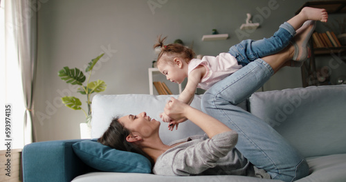 Active caucasian young mom and her little cute daughter playing at home, playing plane on couch. Joyful babysitter working at home - happy family, activity together concept 