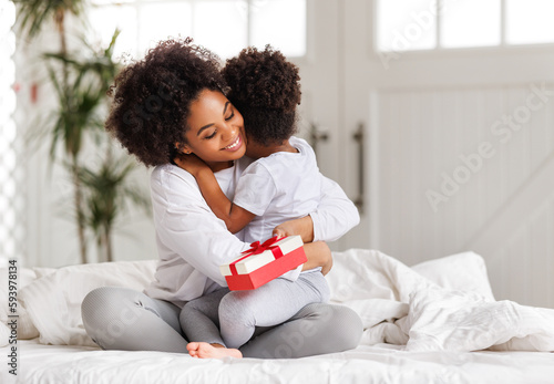 happy mother's day. african american baby daughter giving  gift box to her mom for holiday at home