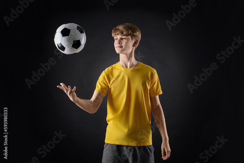 Teenage boy playing with soccer ball on black background