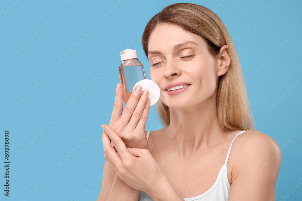 Beautiful woman with makeup remover and cotton pad on light blue background, space for text Beautiful woman with makeup remover and cotton pad on light blue background, space for text
