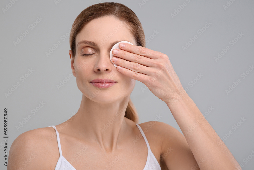 Beautiful woman removing makeup with cotton pad on gray background