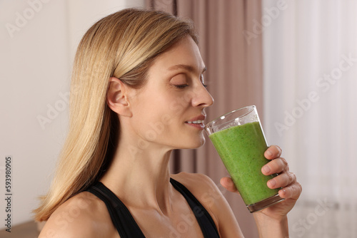 Young woman in sportswear with glass of fresh smoothie at home