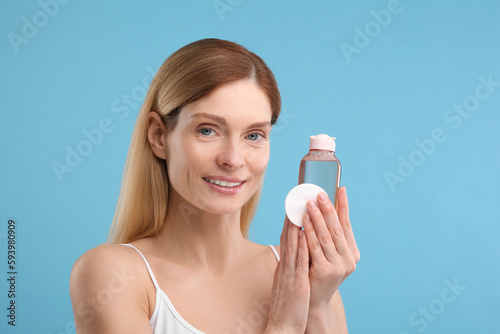 Beautiful woman with makeup remover and cotton pad on light blue background