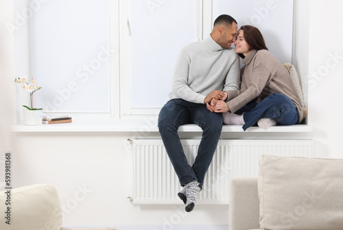 Dating agency. Happy couple holding hands and sitting on window sill at home, space for text