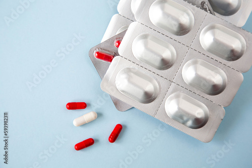 Metallic blister with tablets and pills in red and white are on a blue background.