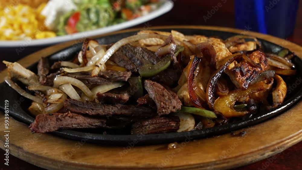 Combination beef and chicken fajitas sizzle on cast iron skillet with peppers and onions, slider close up 4K Combination beef and chicken fajitas sizzle on cast iron skillet with peppers and onions, slider close up 4K
