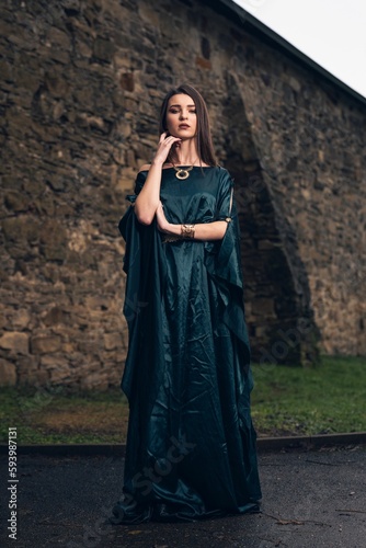 Pretty woman wearing a long dark blue dress and standing in front of the ancient wall