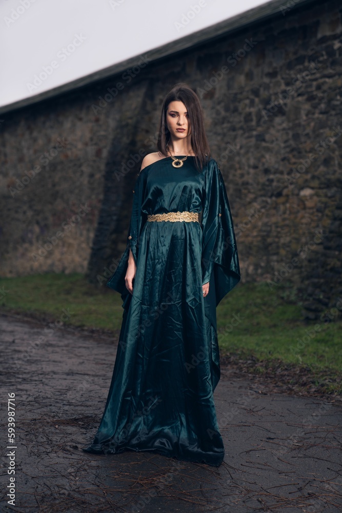 Caucasian woman wearing beautiful dress and standing in front of stony wall Caucasian woman wearing beautiful dress and standing in front of stony wall