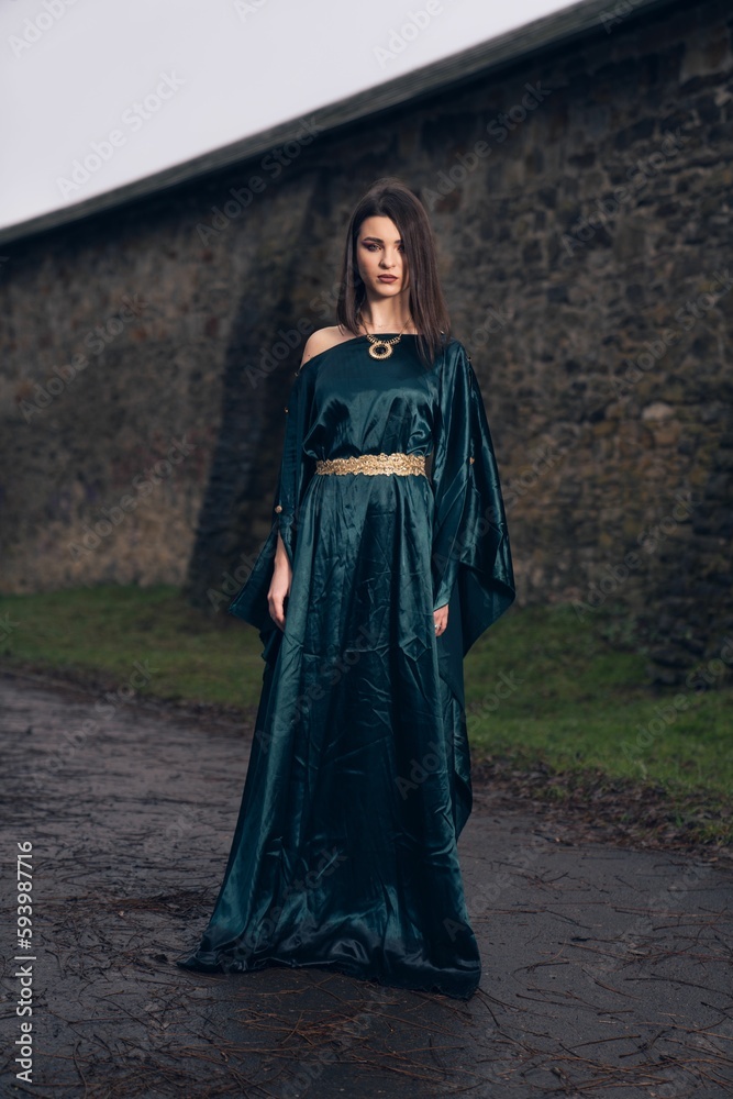 Caucasian woman wearing beautiful dress and standing in front of stony wall