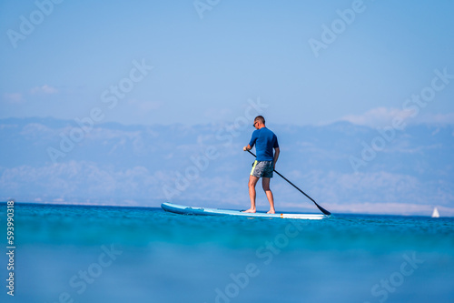 Man riding SUP stand up paddle on vacation.