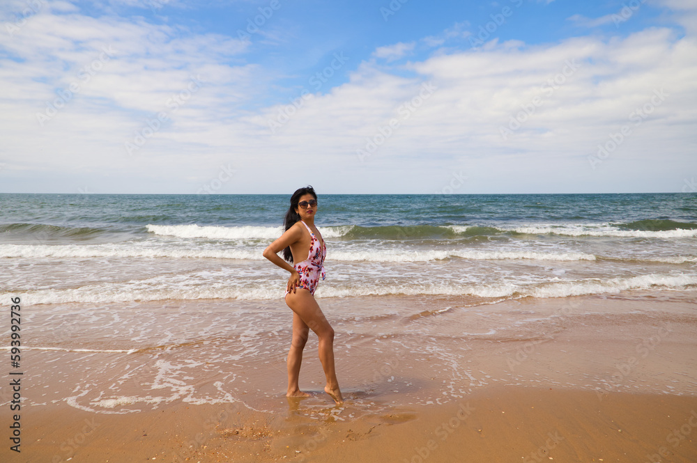 Beautiful and young latin woman is walking along the shore of the beach and posing for photos. Beautiful woman is on holiday on a paradise beach. Holiday and travel concept. Beautiful and young latin woman is walking along the shore of the beach and posing for photos. Beautiful woman is on holiday on a paradise beach. Holiday and travel concept.