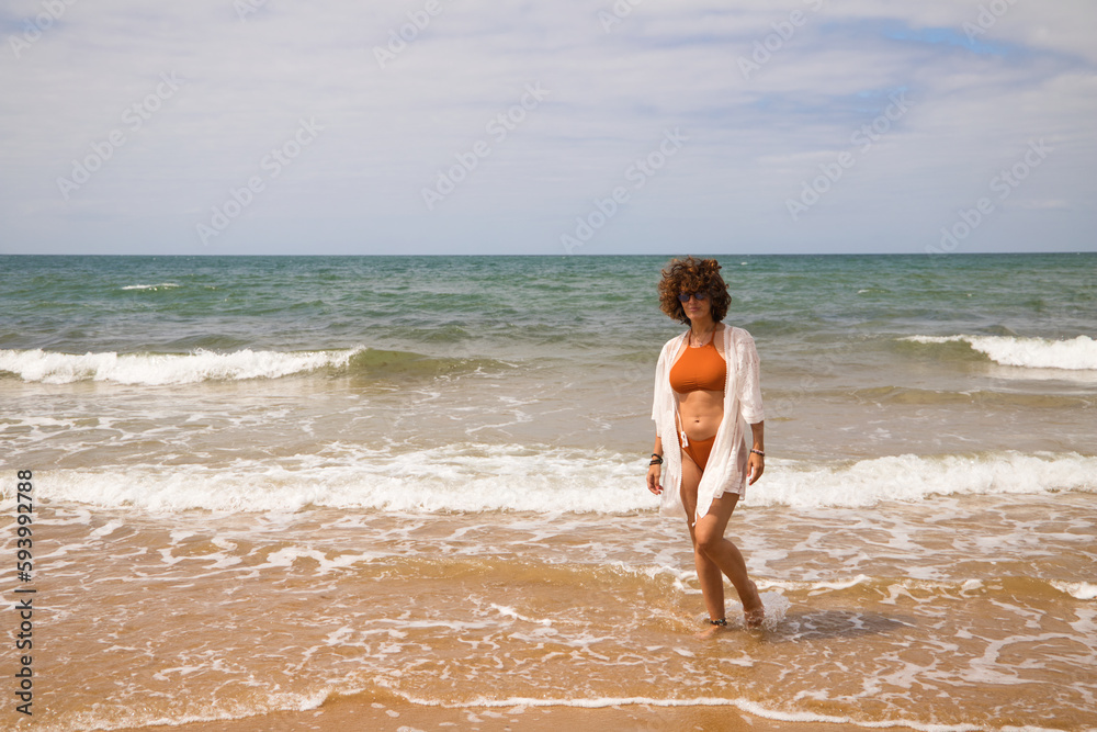 Young beautiful woman in bikini walking along the beach shore. The woman is enjoying her trip to a paradise beach while making different gestures and expressions. Holidays and travels. Young beautiful woman in bikini walking along the beach shore. The woman is enjoying her trip to a paradise beach while making different gestures and expressions. Holidays and travels.