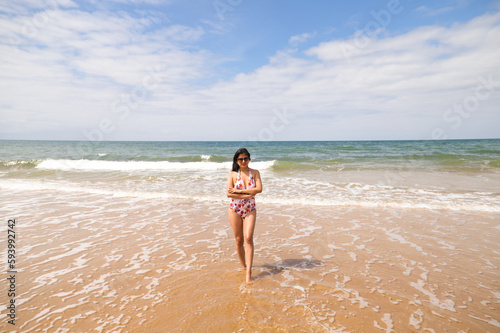 Beautiful and young latin woman is walking along the shore of the beach and posing for photos. Beautiful woman is on holiday on a paradise beach. Holiday and travel concept.