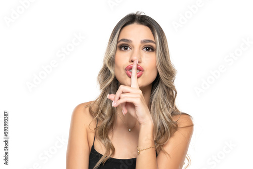 cute woman with long wavy hair holding her finger on her mouth as she was keeping a secret on a white background