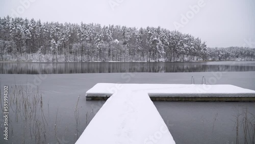Drone footage over a snow-covered dock with a metallic handrail of stairs leading to a lake photo