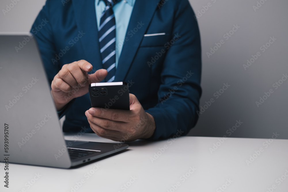Young smart businessman using smartphone while working with laptop in his office room. Young smart businessman using smartphone while working with laptop in his office room.