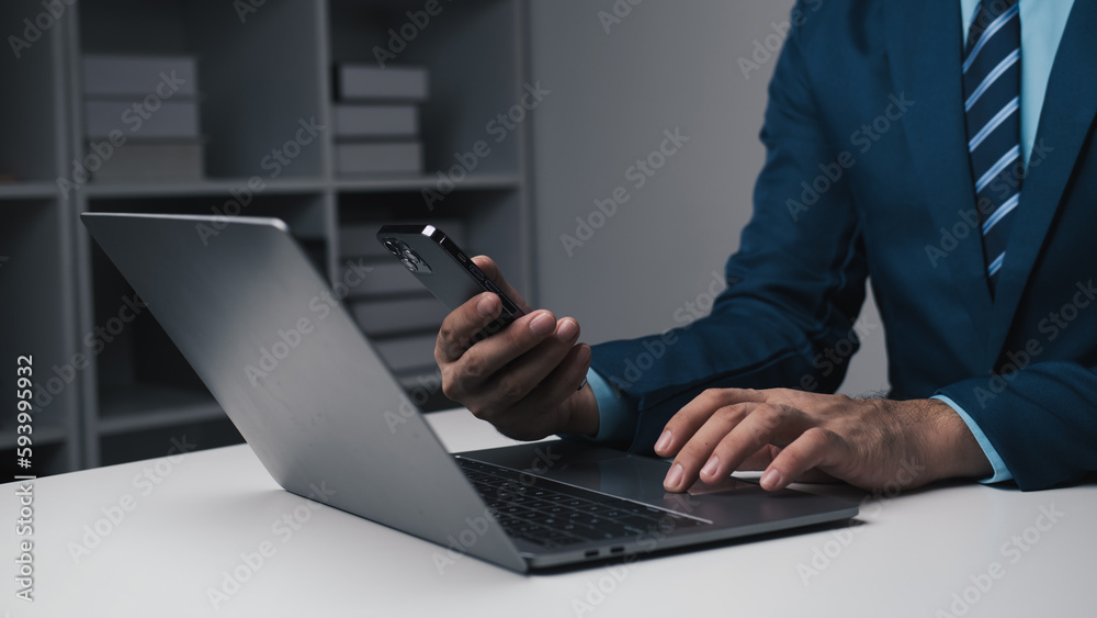 Young smart businessman using smartphone while working with laptop in his office room. Young smart businessman using smartphone while working with laptop in his office room.