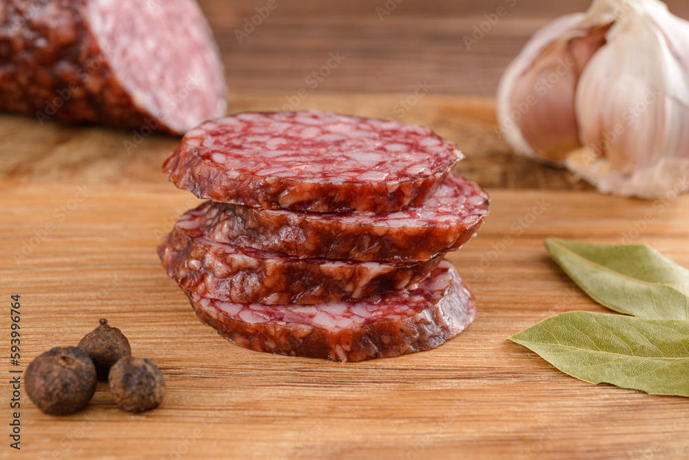 Salami sausage cut slices with garlic, bay leaf and pepper on cutting board