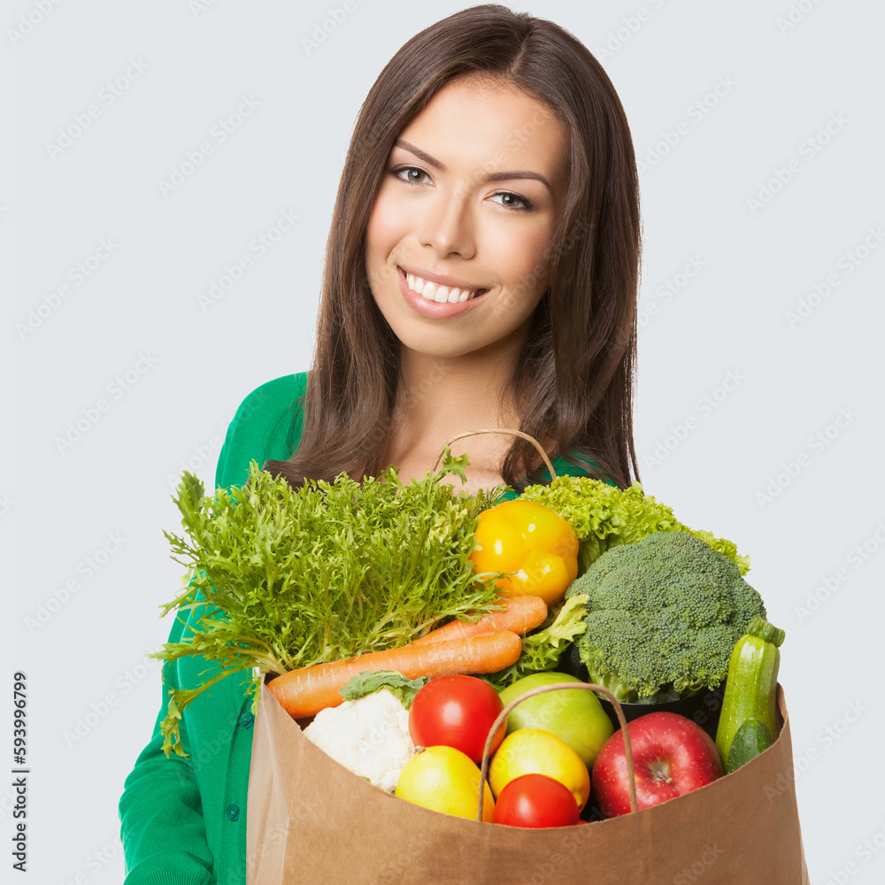 Square image of happy smiling woman in casual wear, green sweater with grocery shopping bag with vegetarian raw food vegetables, isolated on light grey gray background. Healthy eating, dieting Square image of happy smiling woman in casual wear, green sweater with grocery shopping bag with vegetarian raw food vegetables, isolated on light grey gray background. Healthy eating, dieting