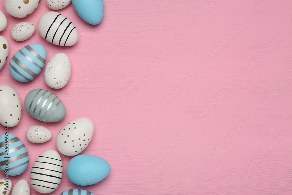 Flat lay composition with festively decorated Easter eggs on pink wooden table. Space for text