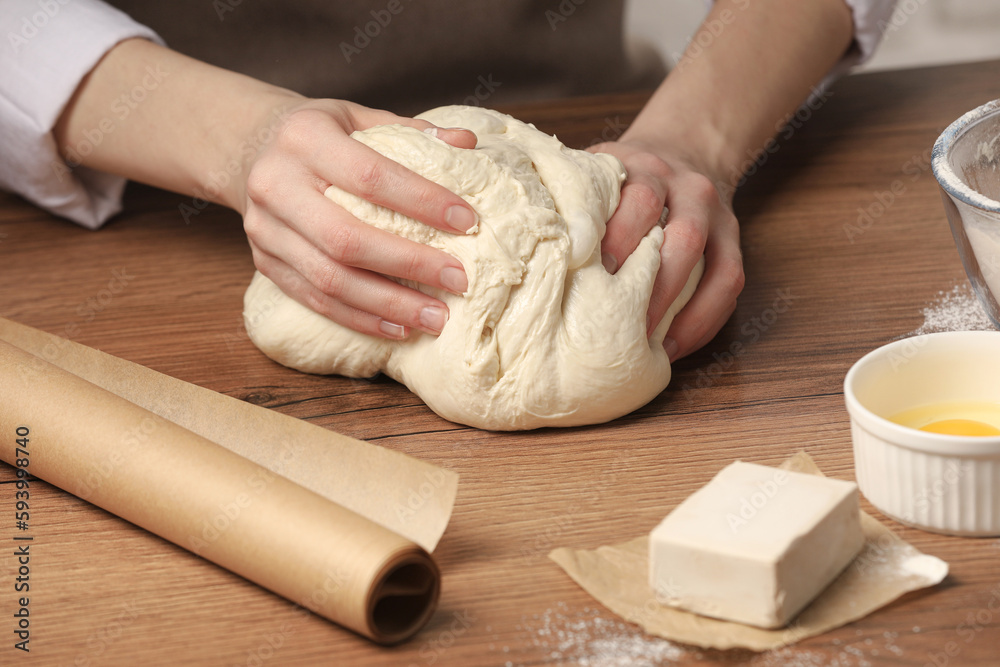 Woman kneading yeast dough for cake at wooden table, closeup