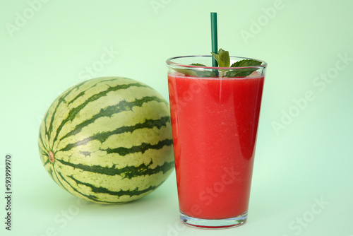 Glass of delicious drink with mint and fresh watermelon on light green background