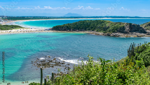 Top view of Praia das Conchas, close to the city of Cabo Frio, with white sand beaches, blue sky, sea with clean waters and in shades of green and blue, with mountains in the background.